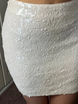 Vit paljettkjol i kort modell - Vit glittrig kjol som har paljetter, Ingen synlig dragkedja eller knappar, bara ren och enkel design. Helt ny med prislapp