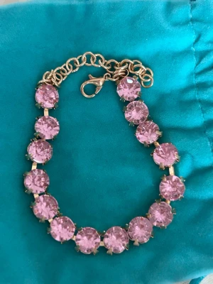 Guldarmband med rosa stenar - Snyggt armband med stora, runda rosa stenar infattade i guldfärgad metall. Armbandet har en klassisk kedja och karbinlås som gör det enkelt att ta på och av. Perfekt för dig som vill ha en färgklick till din outfit.