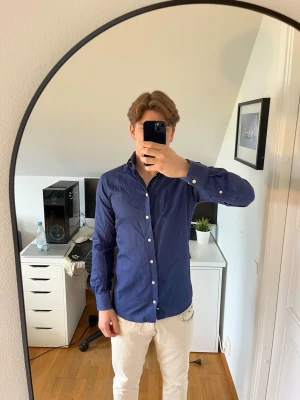 Blå slim fit skjorta från Eton - Snygg blå skjorta från Eton i slim fit-modell. Skjortan har ett diskret mönster, klassisk krage och vita knappar framtill. Tillverkad i 100% bomull.  Bokstäverna N.A är broderade i vänsterarmen (se bild 3)  Hör gärna av dig vid frågor!