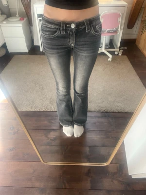 Jeans Gina tricot  - Säljer ett par svarta bootcut jeans med snygga vita kontrastsömmar och slitningar framtill. Jeansen har fem fickor och detaljerade bakfickor med broderi. Perfekta för en trendig och avslappnad look.