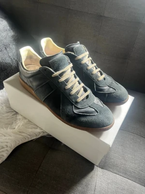 Svarta sneakers i mocka och läder - Snygga svarta sneakers med ovandel i mocka och läder, vita snören och brun gummisula. Klassisk och stilren design som passar till det mesta. Insidan är ljus och skon har en låg profil för en clean look.