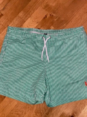 Randiga badbyxor från Polo Ralph Lauren - Två par badbyxor från Polo Ralph Lauren, ett par i grönt och vitt och ett par i rött och vitt, båda med tunna vertikala ränder och dragsko i midjan. Klassisk broderad logga på vänster ben. Perfekta för stranden eller poolen. Skick 9/10
