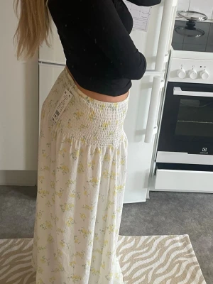 Vit långkjol med blommigt mönster - Säljer en vit långkjol med små gula blommor och smock i midjan! Oanvänd 💛 Strl S🌼🌼