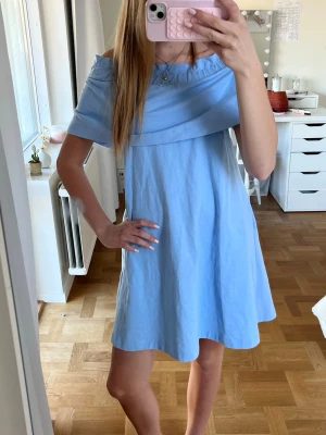 Ljusblå offshoulder klänning - Söt ljusblå offshoulder klänning med volang upptill. Klänningen har en avslappnad passform och är tillverkad i ett mjukt bomullsliknande material. Perfekt för varma dagar och ger en fräsch sommarkänsla.