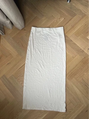 Vit lång kjol från 157 - Lång, rak kjol i vit färg från 157. Kjolen har en enkel och stilren design utan synliga detaljer eller mönster. Tillverkad i mjukt bomullsmaterial som känns bekvämt mot huden. Perfekt för dig som gillar minimalistisk stil. Aldrig  använd fortfarande prislappen på 