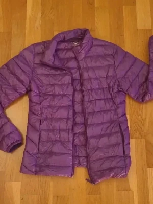 Lila superlätt dunjacka XS - Lila superlätt dunjacka från Cubus i storlek XS. Jackan har quiltad design, dragkedja framtill och fickor med dragkedja. Perfekt nu till våren.