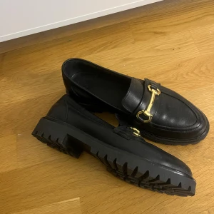 LOAFERS  - Säljer ett par svarta loafers i äkta skinn med chunky sula och snygg guldfärgad metallspänne. Klassisk design med modern twist och chunky sulor! Använda förtal gånger och nypris 1400kr!