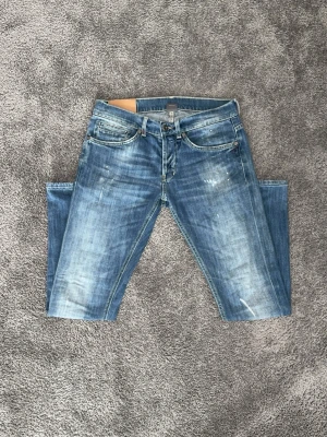 Blå slitna jeans från Dondup - Säljer ett par blå jeans från Dondup med snyggt slitna detaljer och klassisk femficksmodell. Jeansen har raka ben och en tvättad look som ger en avslappnad stil. Materialet är denim i bomull och passformen är normal. Perfekta för dig som gillar en trendig och casual vibe.