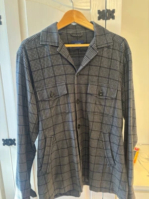 Grå rutig overshirt från Eton - Stilren overshirt från Eton i grått rutmönster. Skjortjackan har klassisk krage, två bröstfickor med knappar och två sidofickor. Tillverkad i mjukt tyg som ger en avslappnad men ändå dressad look. Perfekt lager-på-lager-plagg för en trendig stil. Perfekt för höst .🍂 priser ligger omkring 3000kr. Den är mycket bra skick och priset kan diskuteras privat. Hör gärna av dig om det är några funderingar:)