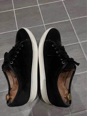 Lanvin skor - Snygga svarta sneakers med både mocka och lackdetaljer. Skorna har vita sulor, svarta skosnören och metallhål för snörningen. Perfekta för dig som gillar en stilren och modern look, storlek 43