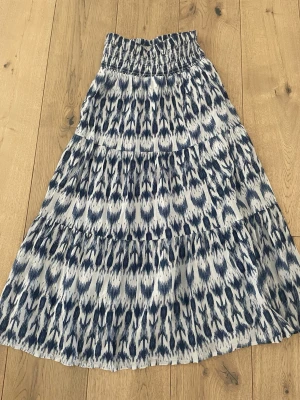 Mönstrad långkjol från Gina Tricot - Säljer en snygg långkjol från Gina Tricot med blått och vitt mönster. Kjolen har resår i midjan och ett flowigt fall som ger en avslappnad vibe. Perfekt för dig som gillar stilrena men ändå unika plagg.