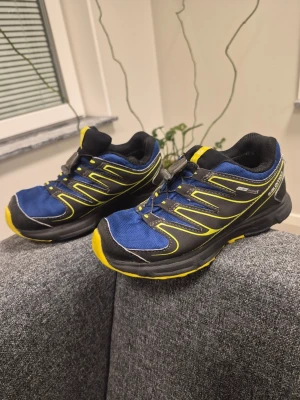 Salomon speedcross Trailskor Blå/Gul Storlek 33 - Säljer ett par sportiga kängor från Salomon i blått och svart med gula detaljer. Skorna har snabbsnörning och robust sula, perfekta för utomhusaktiviteter. Materialet är en mix av textil och syntet, designade för att vara både lätta och tåliga.