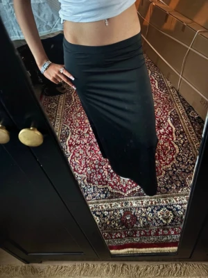 Svart långkjol med slits - Säljer en svart långkjol med slits på sidan. Kjolen har en enkel och stilren design med rak passform. Perfekt att styla med crop tops eller stickade tröjor för en trendig look.