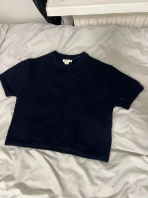 Mörkblå stickad croppad topp - En mörkblå stickad croppad topp med korta ärmar och rund hals. Perfekt för att styla med höga jeans eller kjol. Enkel och stilren design som passar till många olika looks.