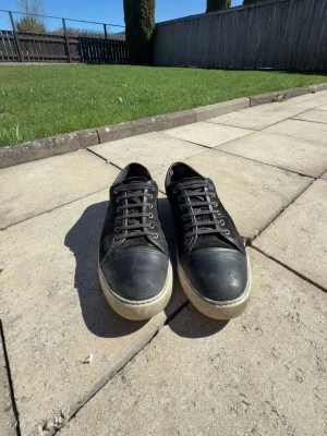 Lanvin skor  - Svarta sneakers med lågt skaft och vit sula. Skorna har svarta skosnören, tåparti i slätt material och sidor i mockaliknande tyg. Perfekta för en avslappnad och stilren look.