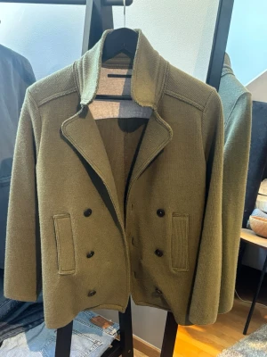 DonDup blazer/cardigan  - Snygg olivgrön stickad blazer/cardigan från det välkända märket DonDup med dubbelknäppning och bred krage. Två framfickor och ribbade detaljer. Perfekt för dig som vill ha en klassisk men ändå avslappnad look.