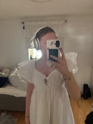 Vit kort klänning  - Säljer en superfin vit kort klänning med puffiga ärmar och v-ringning. Klänningen har snörning framtill och en stor rosett i ryggen vilket gör den justerbar. Perfekt till studenten eller midsommar och har en luftig, flowy passform. Endast provad med prislapp kvar!☀️🙌🏼