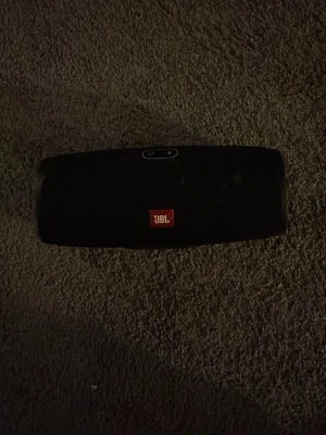JBL Charge 4 Högtalare - Snygg svart bärbar högtalare från JBL med ikonisk logga på framsidan. Högtalaren har cylinderformad design och tydliga knappar för volym, Bluetooth och power på ovansidan. Tillverkad i slitstarkt material med tygfront och gummidetaljer. Perfekt för att ta med överallt. Den är lite smuttsig men det går att tvätta bort om man använder rätt saker den funkar jötte bra fortfarande Bra ljud, Bra Bass, Bra Vibe