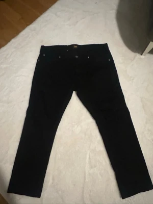 Svarta jeans från Lee - Säljer ett par svarta jeans från Lee med klassisk femficksmodell och raka ben. Jeansen har en diskret Lee-logga på bakfickan och är tillverkade i ett mjukt denimtyg som sitter snyggt. Perfekta till en avslappnad stil.