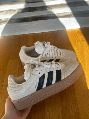 Adidas Samba XLG beige - Skorna är endast provade:) Säljer dessa eftersom de är för små för mig (jag har strl 40) och jag glömde att skicka tillbaka de i tid. De är slutsålda på många hemsidor!  Nypris ca 1500! Adidas Samba XLG skor med en beige ovandel och svarta ränder. Skorna har en brun yttersula och Adidas logotyp finns på plösen.