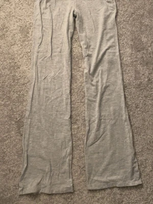 Gråa yoga pants  - Säljer ett par ljusgrå yoga pants med utsvängda ben och nerböjd midja. Byxorna är i mjukt och stretchigt material, perfekta för chill dagar. Inga synliga fickor eller loggor. Passar dig som gillar relaxed och bekväm stil.