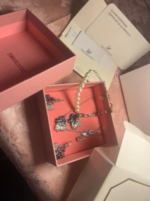 Swarovski smyckeset med pärlor och kristaller ORIGINALPRIS $600 - ORIGINALPRIS $600 har enbart haft dessa i två månader, fick som present, kvittocertifikat kommer med Säljer ett exklusivt smyckeset från Swarovski med matchande örhängen, halsband och armband. Smyckena har silverfärgad metall, gnistrande klara och blå kristaller samt vita pärlor. Kommer i originalask med äkthetsintyg. Perfekt för dig som gillar eleganta accessoarer.