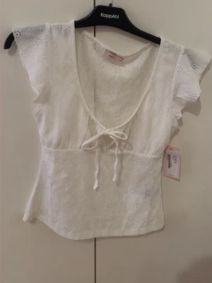 Vit spetsblus med knyt från Nelly  - Söt vit blus i spets från Nelly i storlek M med korta volangärmar, v-ringning och knyt framtill. Fin för sommaren och har aldrig använt den.