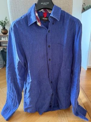Mörkblå linneskjorta från Dahlin - Snygg blå skjorta från Dahlin i 100% linne. Skjortan har klassisk krage, svarta knappar och lång ärm. Perfekt för dig som gillar en stilren och luftig look. Perfekt till sommaren.