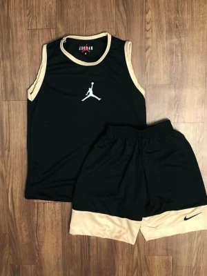 Jordan basketset svart/beige - Snyggt basketset från Jordan med svart linne och matchande shorts. Linnet har beige kantband och en vit Jumpman-logga på bröstet. Shortsen är svarta med beige nederdel och har en svart Nike-logga. Perfekt för basket eller träning.