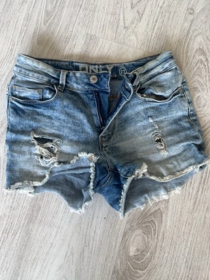 Blå lågmidjade jeansshorts från ONLY - Säljer ett par blå lågmidjade jeansshorts från ONLY med slitna detaljer och fransig kant. Shortsen har klassisk femficksdesign, bälteshällor och dragkedja med knapp. Perfekta för sommaren och ger en avslappnad look💓Kolla in min profil för fler fina och trendiga plagg!