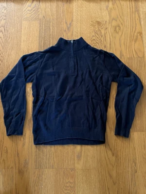 Mörkblå halvzip tröja - Mörkblå stickad tröja med halv dragkedja och hög krage. Tröjan har långa ärmar och ribbade muddar vid ärmslut och nederkant. Perfekt för lager på lager och enkel att matcha med olika outfits.