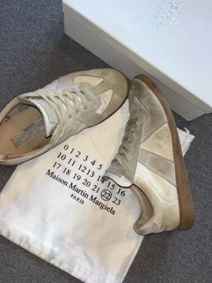 Maisoun mag  sneakers beige - Maison Maghil sneakers i beige mocka och vitt läder med klassisk gummisula. Ikonisk design med märkets signatur på plösen och snygga detaljer i både mocka och läder. Perfekta för dig som gillar stilrena och tidlösa sneakers.