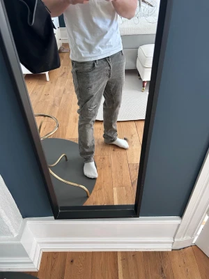 Jack & Jones grå jeans  - Säljer ett par gråa slim fit jeans med klassisk femficksdesign och dragkedjegylf. Jeansen har en snygg tvättad look och sitter tajt över benen för en modern stil. Perfekta till sneakers och t-shirt för en avslappnad vibe.