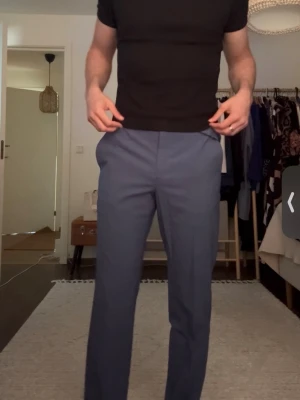 Blå kostymbyxor  - Snygga blå kostymbyxor med raka ben och pressveck. Byxorna har bälteshällor, två sidofickor fram och två bakfickor med knapp. Perfekta för en clean och stilren look. Materialet ser ut att vara en klassisk kostymblandning.