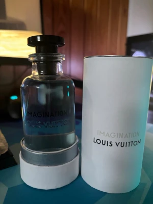 Imagination parfym från Louis Vuitton - Imagination från Louis Vuitton är en exklusiv parfym i en elegant, genomskinlig glasflaska med svart lock. Flaskan har en stilren och modern design och kommer med en vit, rund förpackning med silverdetaljer och tryckt logotyp.