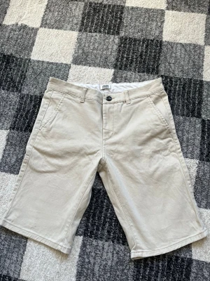 Beige shorts från Jack & Jones - Säljer ett par klassiska beige shorts från Jack & Jones. De har normal passform, midwaist och är tillverkade i bomull. Perfekta för sommarens alla äventyr.