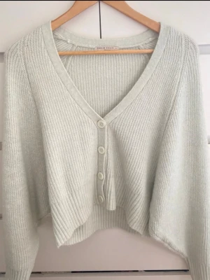 stickad kofta  - Superfin ljus stickad kofta i mjukt material. Croppad modell med V-ringning och knappar framtill. Perfekt till både jeans och kjol för en clean look. Använd få gånger, i mycket fint skick. Storlek L men sitter som m/s