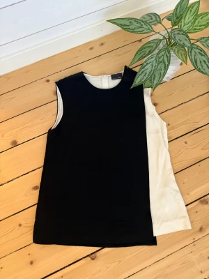 Svart och vit ärmlös linnetopp -  Fendi - Snygg ärmlös linnetopp i svart och vitt med rak passform och rund halsringning. Toppen har en cool tvåfärgad design där ena sidan är svart och den andra vit. Perfekt att styla med jeans eller kjol för en trendig look. Enligt bild…. Småstorlek 34, 36, 38. 