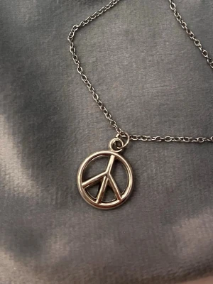 Peace halsband peacemärke silver imitation  - Fint halsband med en berlock i form av ett peace märke. Berlocken är ca 1,5 cm i diameter. Trädd på kedja i silverimitation som är justerbar 40-45 cm. 