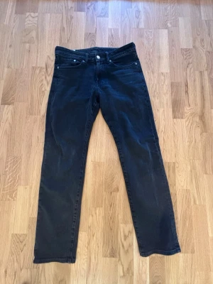Svarta raka jeans - Snygga svarta jeans från H&M med rak passform och klassisk femficksdesign. Jeansen har normal midja och stängs med dragkedja och knapp. Perfekta för en stilren och enkel look.