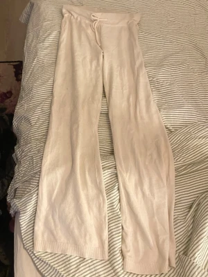 Beige mjukisbyxor med dragsko - Säljer ett par beige mjukisbyxor med breda ben och dragsko i midjan. Byxorna är gjorda i ett mjukt och stretchigt material, perfekta för att chilla hemma. Ribbad kant vid benslut och hög midja för extra komfort.