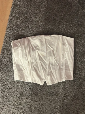 Vit tubtopp - Säljer en stilren vit tubtopp med lätt struktur framtill och smockad baksida för extra komfort. Toppen är axelbandslös och har en enkel, clean look som passar perfekt till jeans eller kjol. 🤍