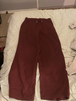 Vinröda mjukisbyxor med vida ben - Säljer ett par vinröda mjukisbyxor med breda ben och låg midja. Byxorna har två stora fickor framtill och elastisk midja med dragsko. Perfekta för chill dagar och riktigt skön passform.