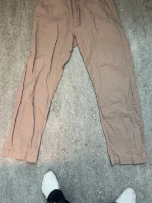 Beiga mjukisbyxor från 157 - Säljer ett par beiga linnebyxor från 157 med dragsko i midjan och avslappnad passform. Byxorna har resår i midjan och raka ben. Perfekta för chill dagar och riktigt sköna att ha på sig.