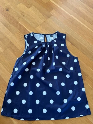 Prickig blus  - Snygg och klassisk blus med vita prickar.  Ärmlös blus med fin detalj vid halsen. Lätt och skönt material.