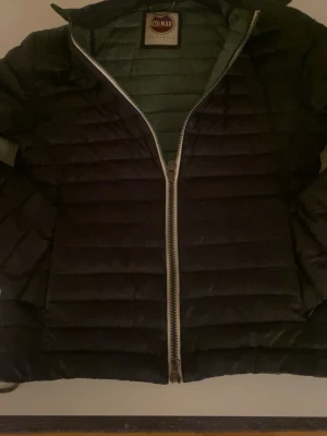 Svart dunjacka från Colmar - Säljer en svart dunjacka från Colmar med quiltad design och dragkedja framtill. Jackan har en hög krage och är lätt vadderad för extra värme. Perfekt för kalla vinterdagar och har en stilren look som passar till det mesta.