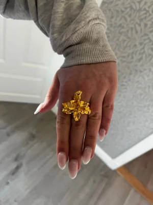 BLOMRING I GULD FÄRG - Cool och unik ring i guldtonat metall med en stor,  blomma som ser lite ut som blomman i Rapunzel/Trasel. Aldrig andvänd, helt nyskick! Jätte fin ring för dig som inte vill vara så basic. Passar perfekt till alla stilar men speciellt Stockholms stil där man ofta har lite större ringar som faktiskt syns. Sitter jätte fint på fingret och du kan ändra storleken. Fick den i present men jag andvänder silver, inte guld. Annars hade jag gärna behållit den! 💞🌼