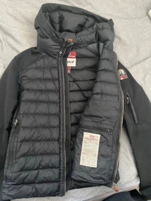 Svart dunjacka från Parajumpers - Snygg svart dunjacka från Parajumpers med huva och quiltad design. Jackan har dragkedja framtill, praktiska fickor och en patch med Parajumpers-logga på ärmen. Hör av er vid funderingar. 