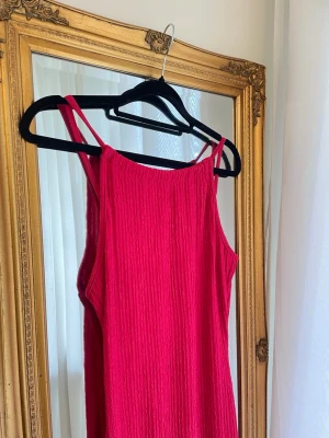 Rosa sommarklänning med smala axelband - Snygg röd klänning med smala justerbara axelband och rak halsringning. Klänningen är gjord i ett lätt, krinklat tyg storlek S oanvänd, slits på båda sidorna 