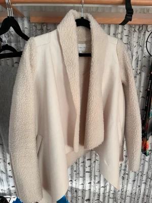 Krämvit teddyjacka från Cotton On - Säljer en krämvit teddyjacka från Notion 1.3 med oversized krage och mjukt, fluffigt material. Jackan har öppen front, långa ärmar och en avslappnad passform. Perfekt för dig som gillar mysiga och trendiga ytterplagg.